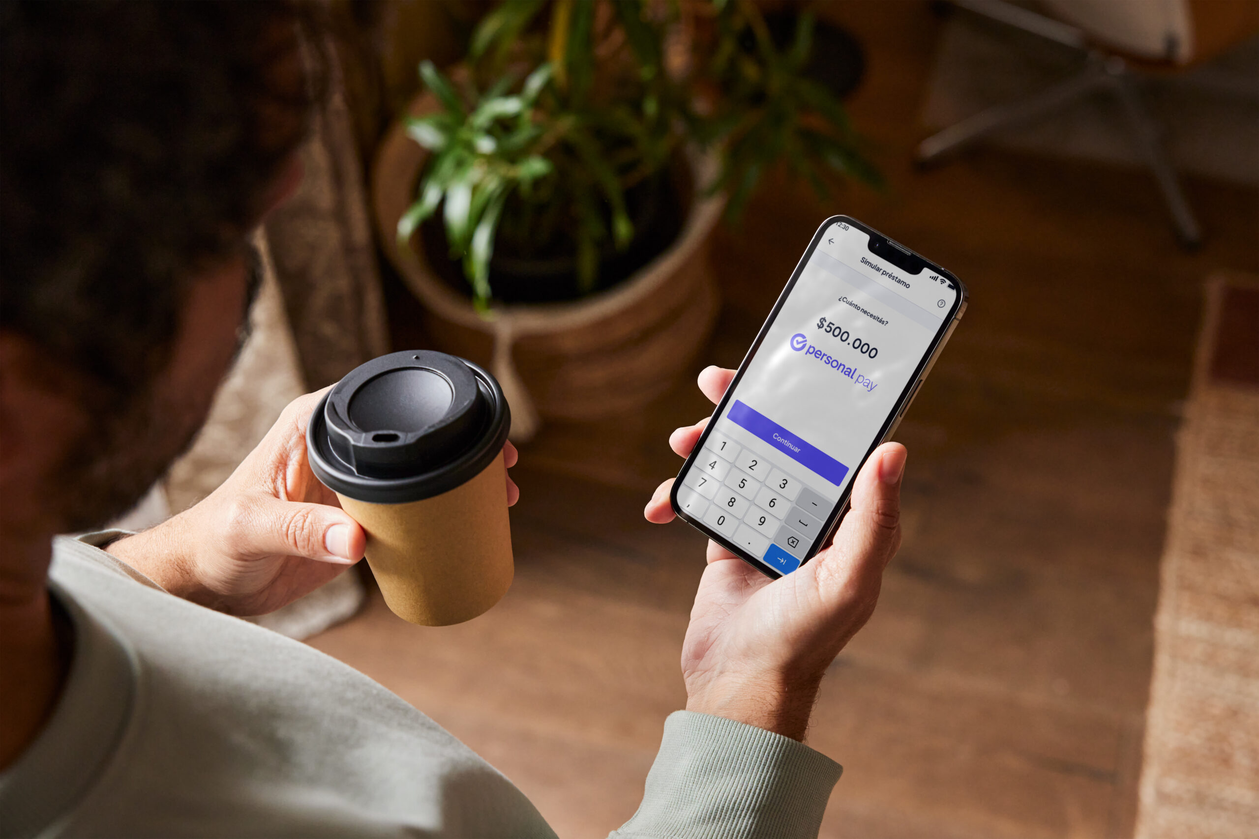 Persona utilizando la app de Personal Pay en el celular para solicitar un préstamo mientras sostiene un café