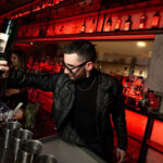 Bartender preparando cócteles en una barra iluminada con botellas de fondo durante una experiencia de coctelería en Malasangre