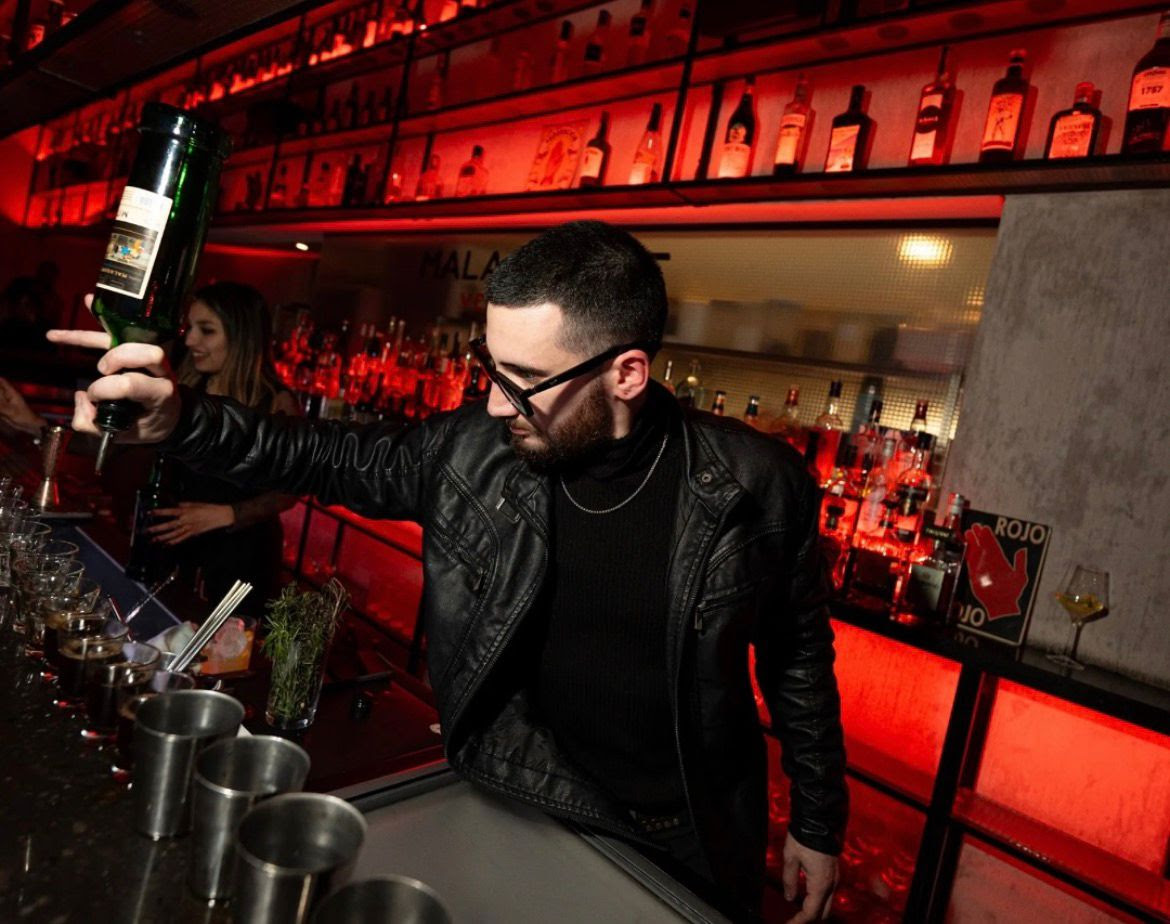 Bartender preparando cócteles en una barra iluminada con botellas de fondo durante una experiencia de coctelería en Malasangre