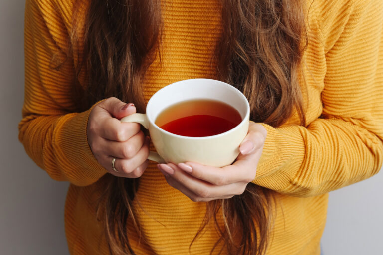 Mujer con sweater amarillo sosteniendo una taza de té caliente en una escena cálida y relajante para el Día Internacional del Té