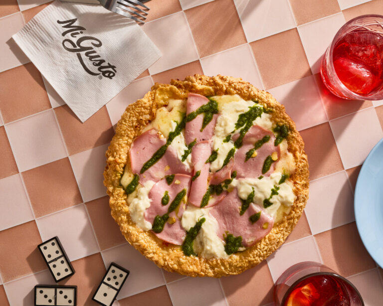 Pizza sin gluten con jamón y mozzarella servida sobre mesa con bebida y ambientación casual en restaurante argentino