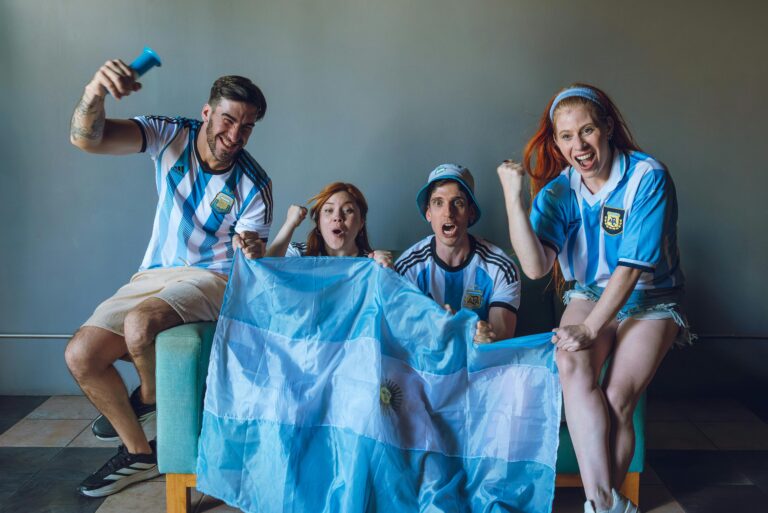 Grupo de jóvenes con camisetas de la selección argentina celebrando frente a una pantalla y sosteniendo una bandera, en una escena vinculada al clima mundialista y la cultura laboral