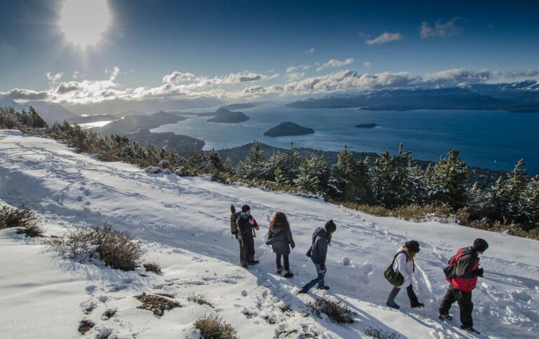 Turistas recorren un sendero nevado con vistas al lago y a las montañas de la Patagonia, en uno de los paisajes más emblemáticos de Río Negro durante el invierno