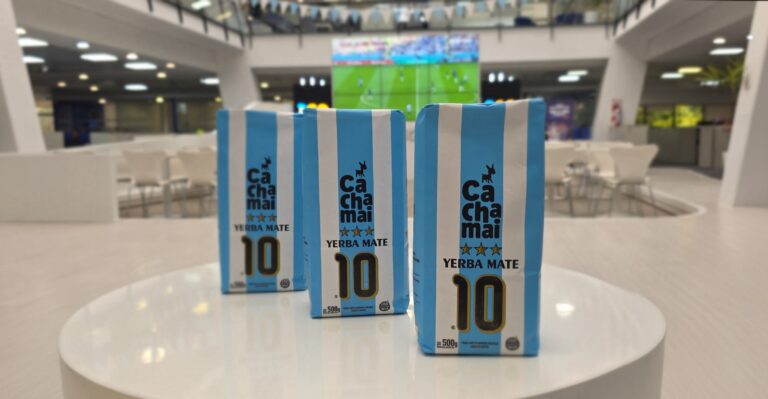 Paquetes de Cachamai Yerba Mate 10 con diseño inspirado en los colores de la selección argentina, exhibidos frente a una pantalla con un partido de fútbol en un ambiente mundialista