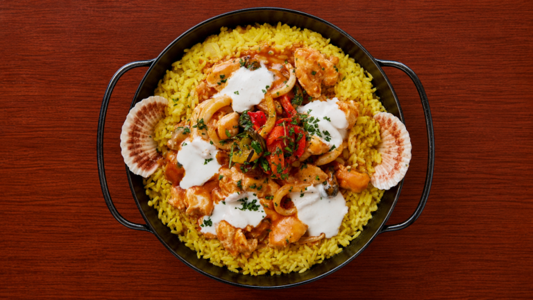 Paella de arroz amarillo con mariscos, vegetales y salsa cremosa, servida en sartén de hierro durante el pop up de cocina española de A Coruña en El Patio de Mabel