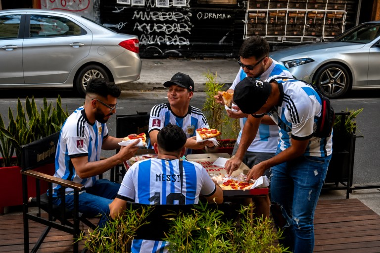 Grupo de amigos comparte pizzas estilo New York en una mesa al aire libre durante una celebración por el Día del Amigo en Hell’s