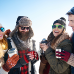 Grupo de cuatro amigos abrigados comparte bebidas calientes y un momento de recreación durante las vacaciones de invierno en un paisaje nevado