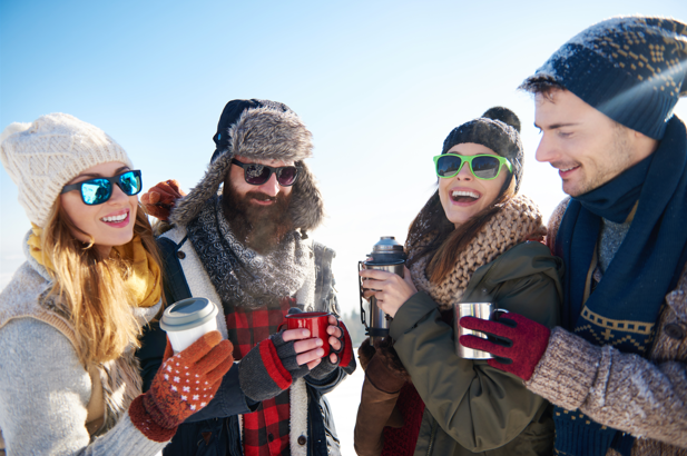 Grupo de cuatro amigos abrigados comparte bebidas calientes y un momento de recreación durante las vacaciones de invierno en un paisaje nevado