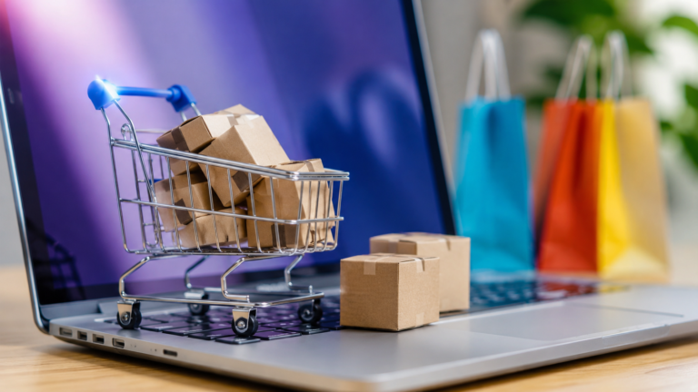 Carrito de compras con paquetes sobre una computadora portátil, representando las ventas online y el comercio electrónico