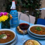 Guisos de lentejas servidos en platos junto a una botella de Sifón, pan y una copa de vino