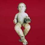 Escultura de un niño sentado sobre fondo rojo, atribuida a Miguel Ángel y conservada en el anonimato por una familia argentina, cuya autenticidad aún debe confirmarse