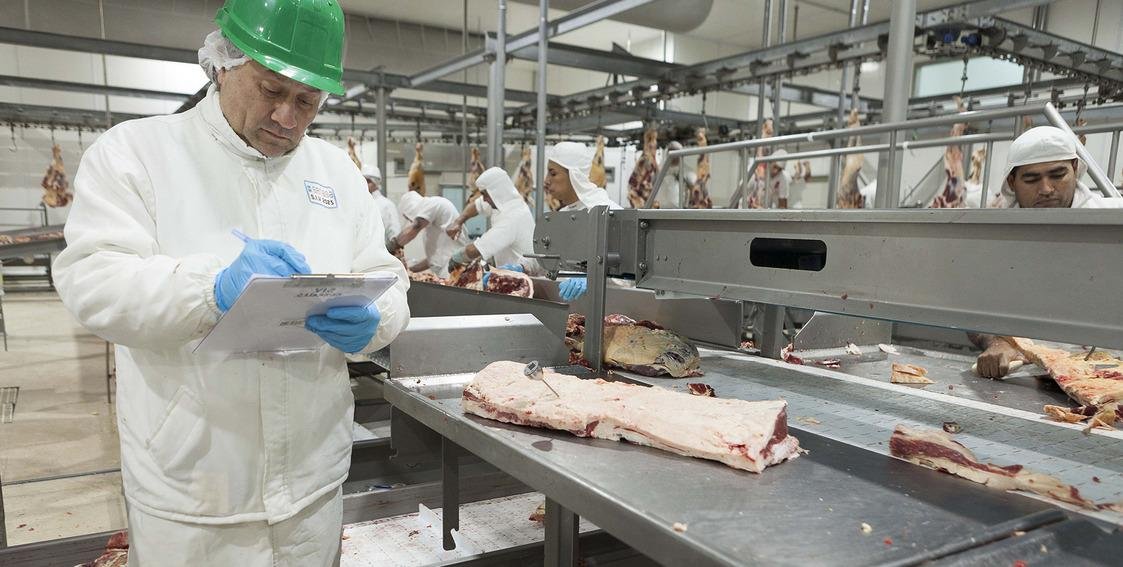 Inspectora sanitaria revisa productos cárnicos en una planta de procesamiento de alimentos, ilustrando los controles internacionales sobre exportaciones argentinas